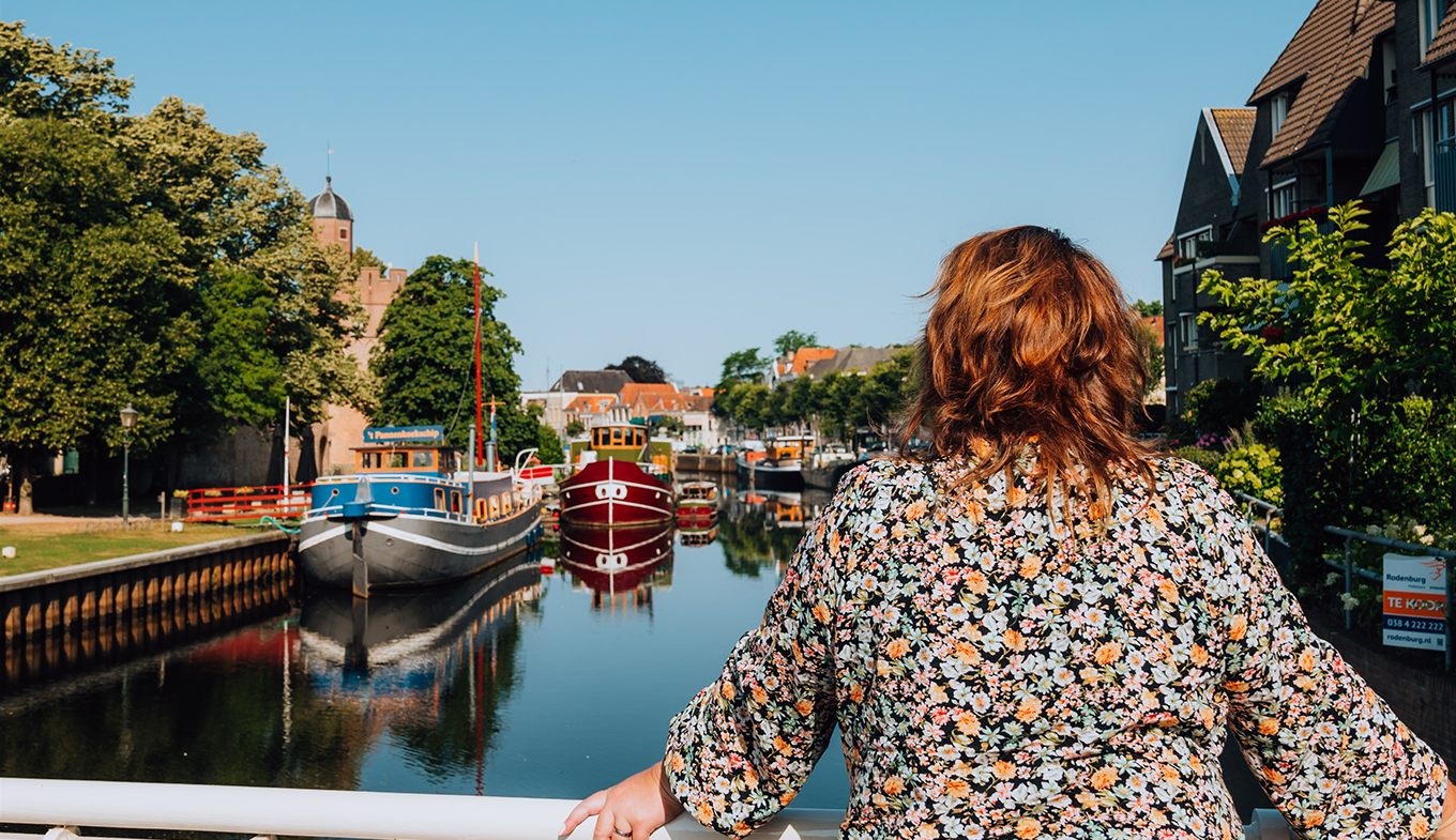 Vrouw leunt op brugreling en kijkt uit over water waarop boten aangemeerd liggen. Vrouw leunt op brugreling en kijkt uit over water waarop boten aangemeerd liggen.