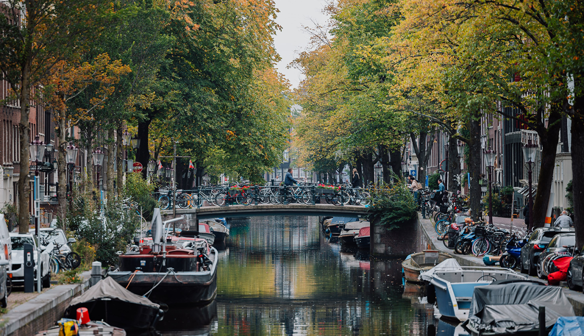 Beeld over gracht met aangelegde bootjes, waarbij verderop een man over een bruggetje fietst Beeld over gracht met aangelegde bootjes, waarbij verderop een man over een bruggetje fietst