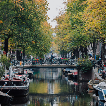 Beeld over gracht met aangelegde bootjes, waarbij verderop een man over een bruggetje fietst