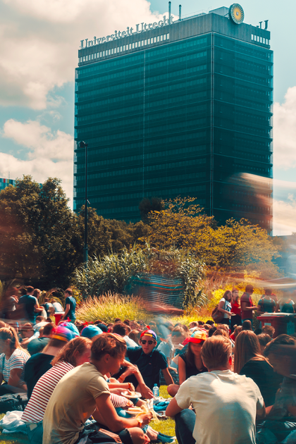 Studenten zitten op een grasveld in Utrecht Science Park, met op de achtergrond Universiteit Utrecht zichtbaar