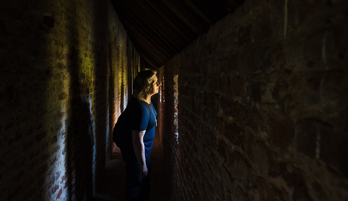In een donkere gang valt licht binnen, waardoor we een vrouw naar buiten zien kijken In een donkere gang valt licht binnen, waardoor we een vrouw naar buiten zien kijken