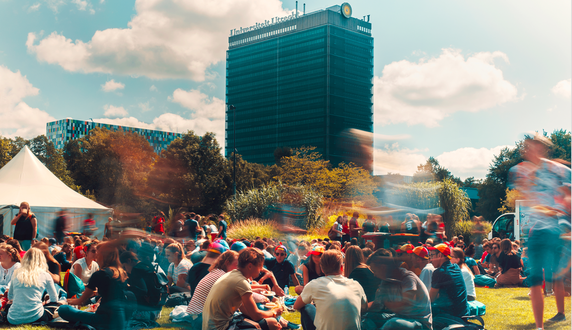 Studenten zitten op een grasveld in Utrecht Science Park, met op de achtergrond Universiteit Utrecht zichtbaar
