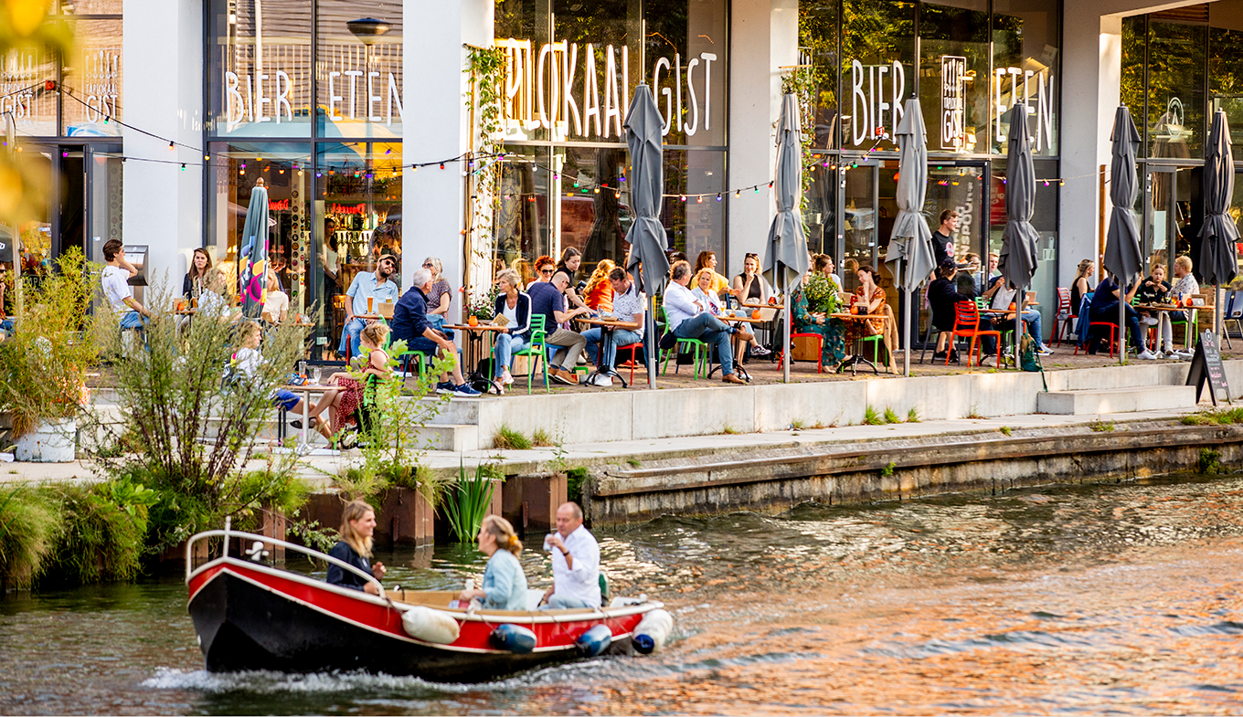 Bootje met twee mensen vaart voor een vol terras langs over een Utrechtse gracht. Bootje met twee mensen vaart voor een vol terras langs over een Utrechtse gracht.