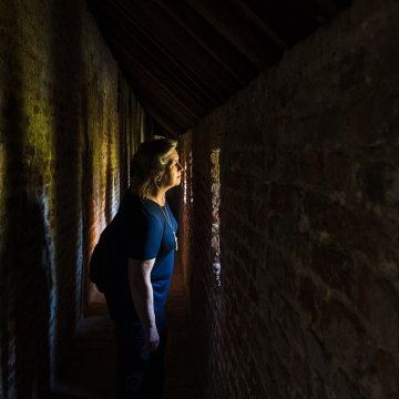 In een donkere gang valt licht binnen, waardoor we een vrouw naar buiten zien kijken