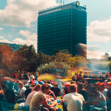 Studenten zitten op een grasveld in Utrecht Science Park, met op de achtergrond Universiteit Utrecht zichtbaar