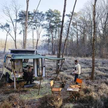 In een stuk bos met rijp op de begroeiing zien we een mini-caravan met een stel dat iets warms drinkt.