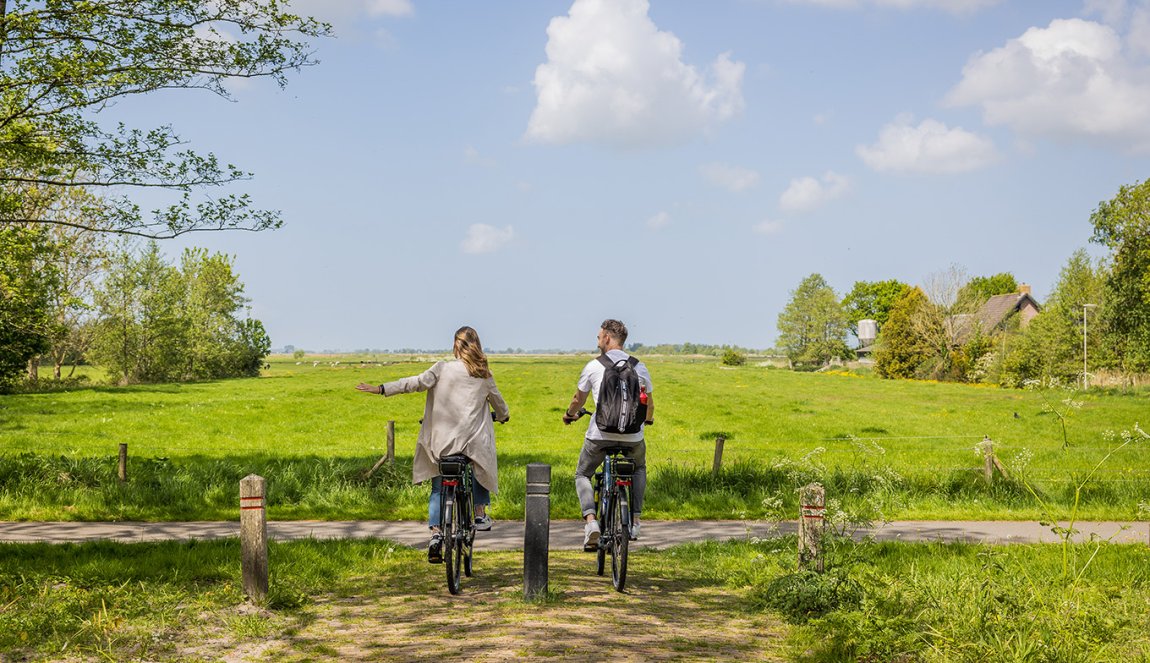 Stel fiets door het Friese landelijk gebied en steekt hand uit Stel fiets door het Friese landelijk gebied en steekt hand uit