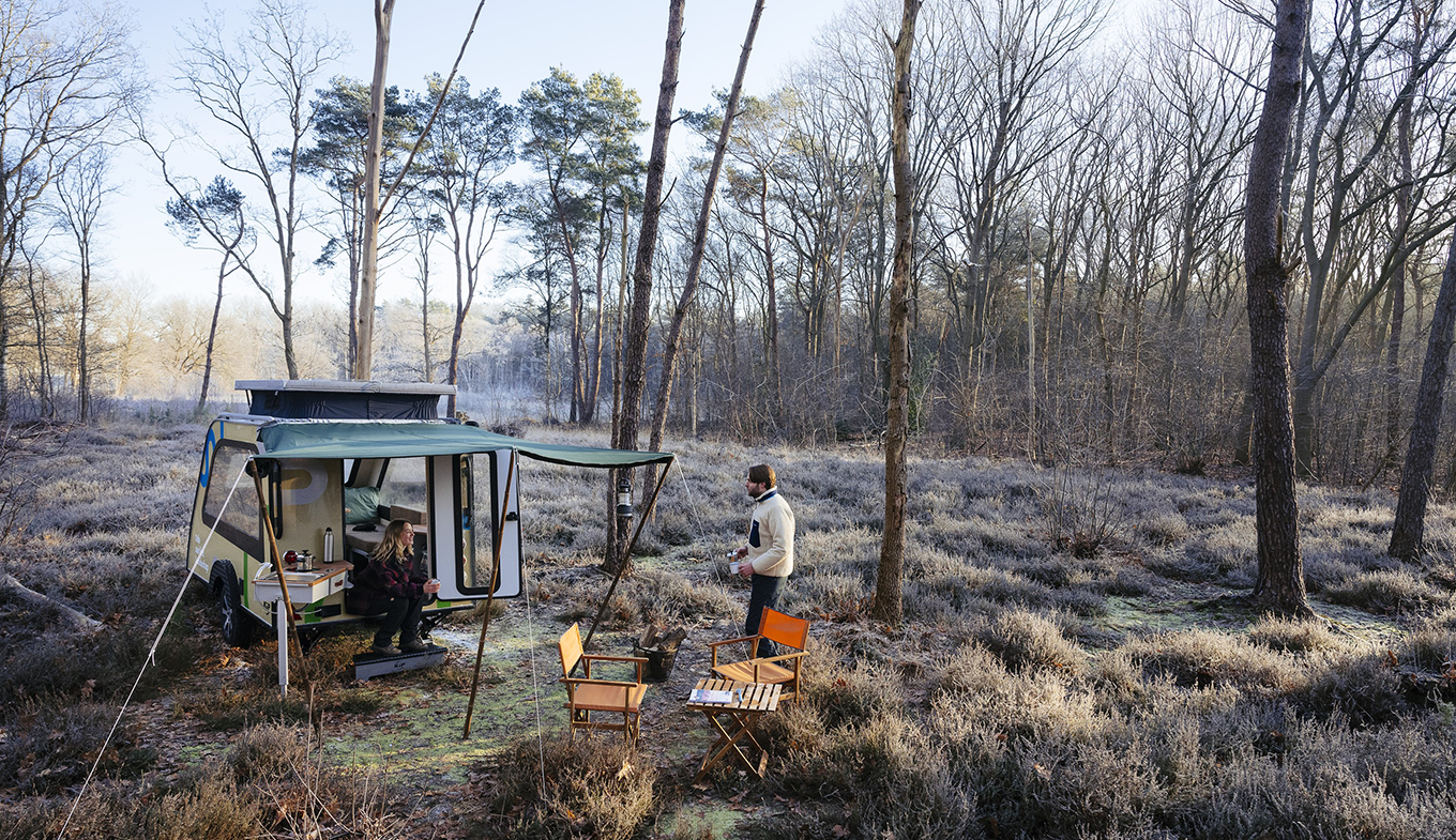 In een stuk bos met rijp op de begroeiing zien we een mini-caravan met een stel dat iets warms drinkt. In een stuk bos met rijp op de begroeiing zien we een mini-caravan met een stel dat iets warms drinkt.